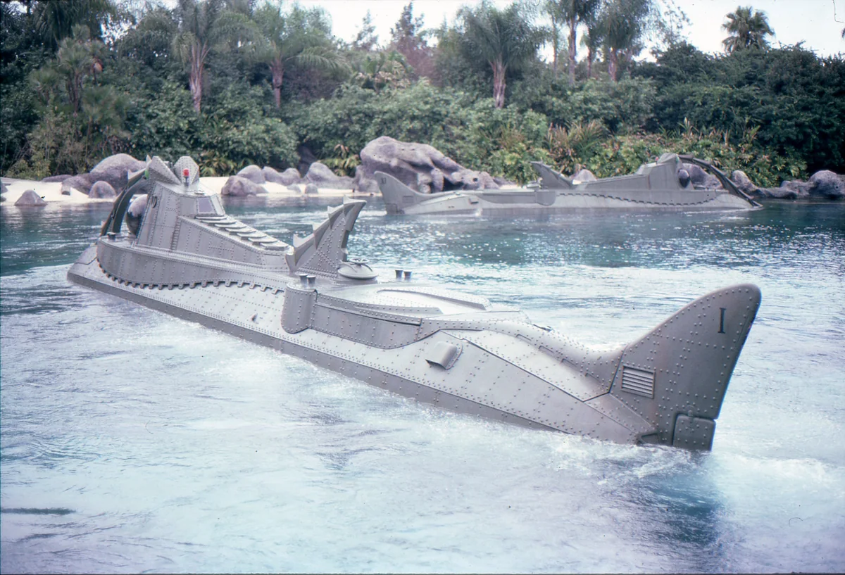 Two gray Nautilus-style submarines in a lagoon bordered by rocks and palms.